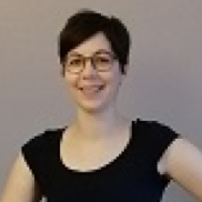 Junge Frau mit kurzem Haar und Brille, trägt ein schwarzes Oberteil, lächelt freundlich.